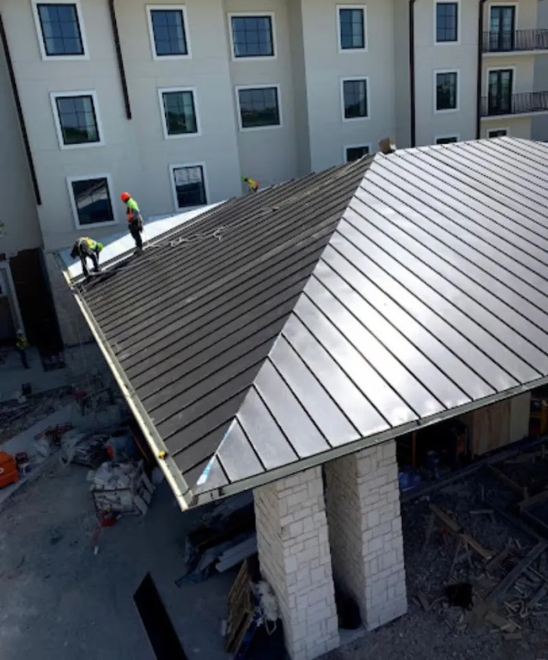 Crew installing standing seam metal roof panels on a commercial project in Prosper